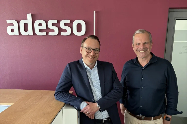 Mario Zillmann, Senior Partner bei Lünendonk, und Peter de Lorenzi, Geschäftsführer der adesso as a service GmbH, stehen gemeinsam vor dem adesso-Logo und lächeln in die Kamera.