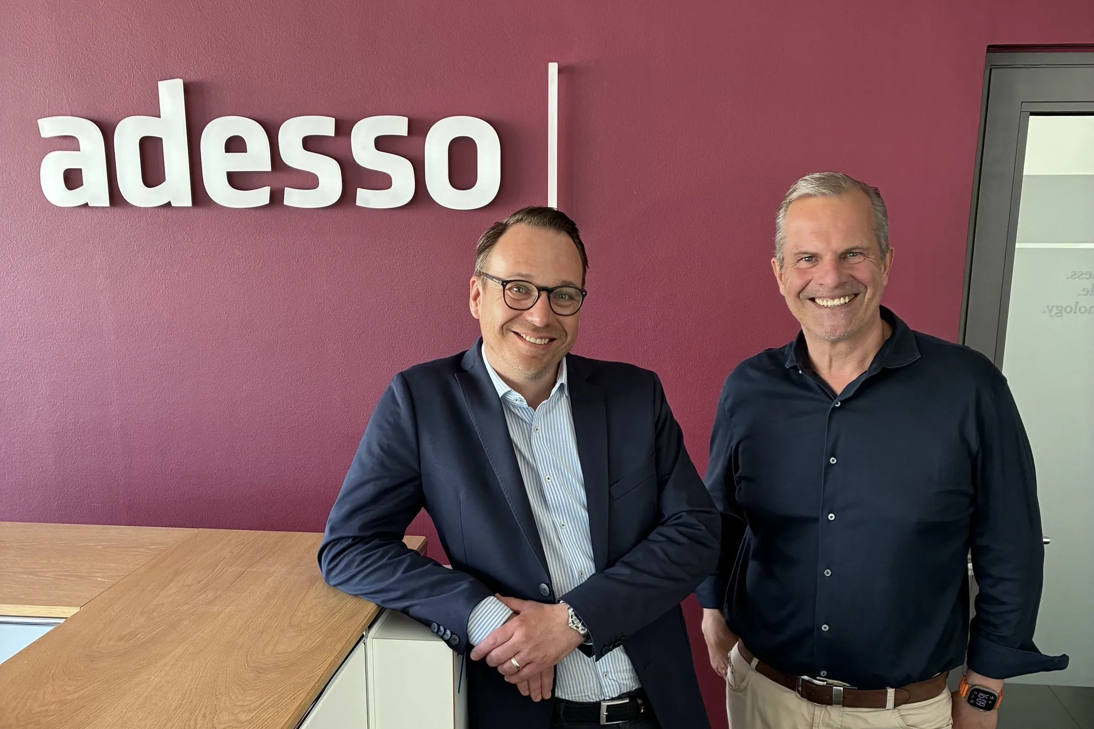 Mario Zillmann, Senior Partner bei Lünendonk, und Peter de Lorenzi, Geschäftsführer der adesso as a service GmbH, stehen gemeinsam vor dem adesso-Logo und lächeln in die Kamera.