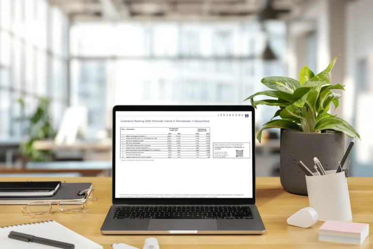 Laptop auf einem Holzschreibtisch zeigt das Lünendonk-Ranking 2026: Führende interne IT-Dienstleister in Deutschland – eine Tabelle mit den Top-10-Unternehmen nach Gesamtumsatz und Mitarbeiterzahl. Im Hintergrund ein helles Büro, daneben eine Zimmerpflanze, Notizbücher, eine Brille und Stifte.